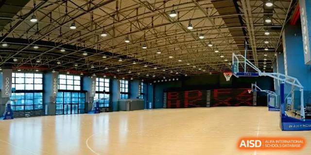 An interior view of the large, well-lit indoor basketball gymnasium at the Affiliated High School Of Peking University Haikou.
