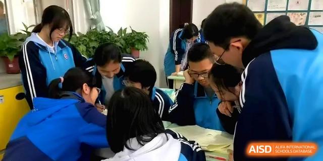 Students in blue uniforms huddle together over a desk, intensely focused on a collaborative group project and shared notes at Baoji Nanshan High School.