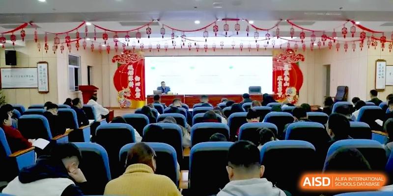 An audience of students sits in a large, modern auditorium with red decorations, watching a presentation on a wide stage at Baoji Nanshan High School.