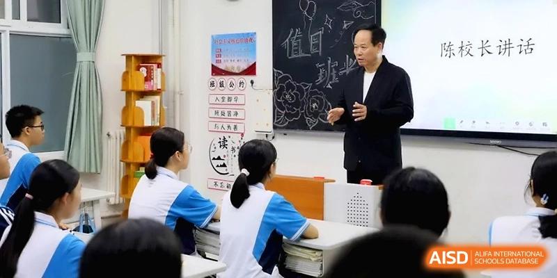 An educator in a dark suit stands before a chalkboard, gesturing while leading a focused academic discussion with his students at Baoji Nanshan High School.