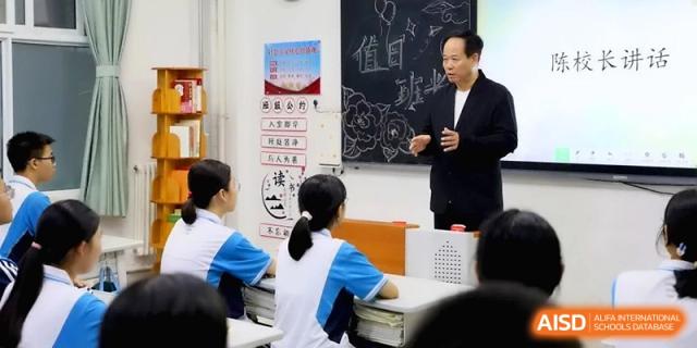 An educator in a dark suit stands before a chalkboard, gesturing while leading a focused academic discussion with his students at Baoji Nanshan High School.