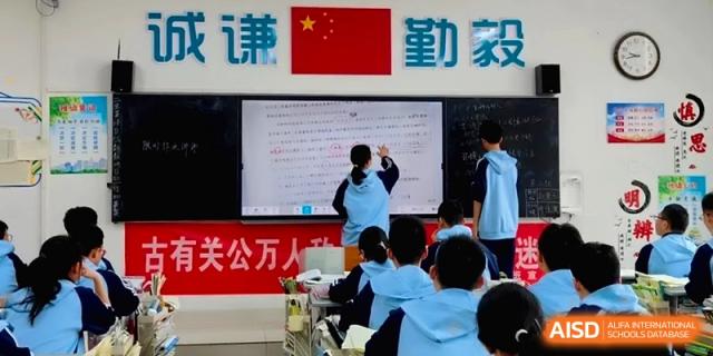 A student stands at a large digital screen at the front of the classroom, presenting a detailed lesson to her seated peers at Baoji Nanshan High School.