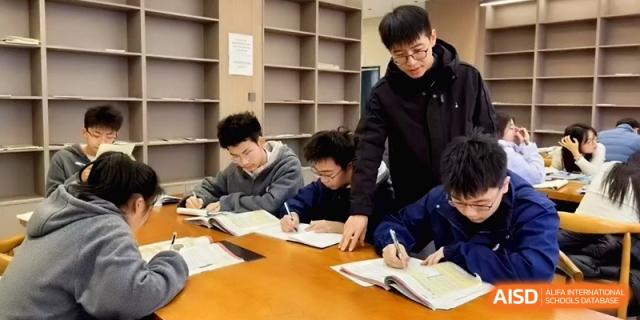 A group of students sits at a long wooden table in a library, diligently writing in their notebooks and studying together at Baoji Nanshan High School.