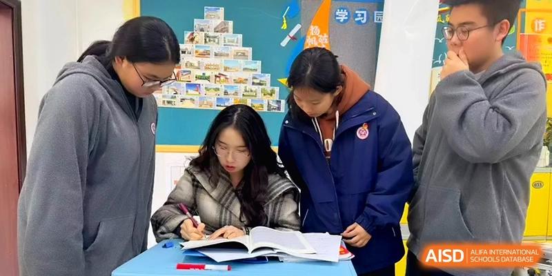 Students gather around a desk to review a textbook during an interactive group study session in a bright classroom at Baoji Nanshan High School.