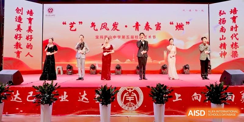 Formally dressed students stand on a decorated stage with microphones for a cultural performance or ceremony at Baoji Nanshan High School.