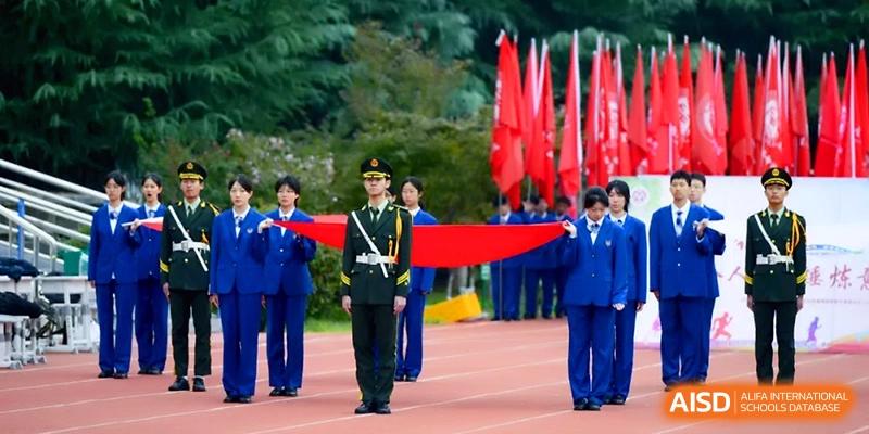 Students in blue uniforms perform a formal flag-bearing ceremony on a red running track during a school event at Baoji Nanshan High School.