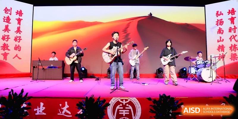 A student band featuring guitarists and a lead singer performs under vibrant stage lighting during a school concert at Baoji Nanshan High School.