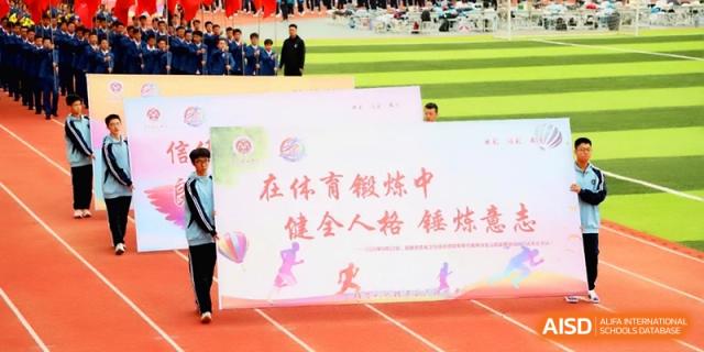 Students carry a large white banner with inspirational Chinese text across an athletic field during a sports meet at Baoji Nanshan High School.