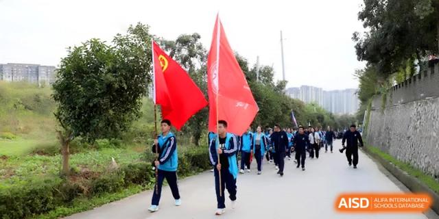 Male students march proudly while carrying large red flags down a campus path during a celebratory outdoor parade at Baoji Nanshan High School.