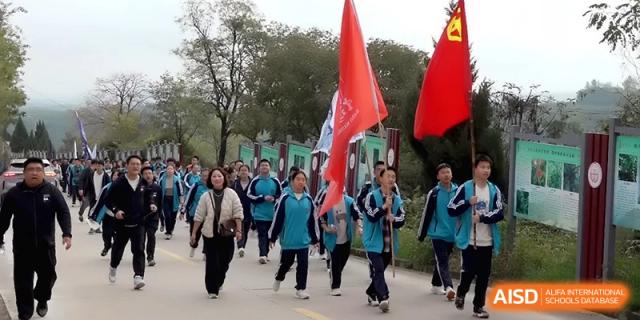 A large group of students and faculty members walks together during an outdoor marching activity carrying flags at Baoji Nanshan High School.