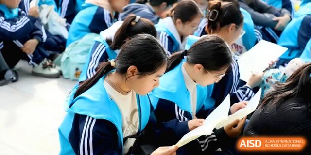 Students in blue and white uniforms lean forward to focus on their handouts during an outdoor academic or social event at Baoji Nanshan High School.