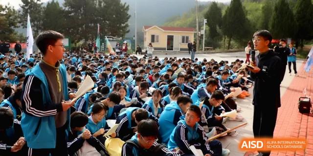 A vast crowd of students sits together on the ground outdoors during a large-scale school assembly or presentation at Baoji Nanshan High School.