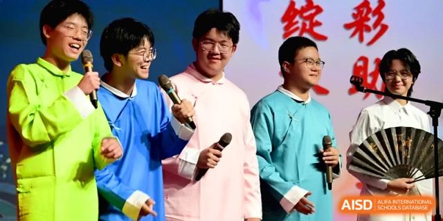 Three male students in traditional blue and pink robes hold microphones and smile during a stage performance at Baoji Nanshan High School.