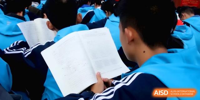 A close-up view of a student holding an open textbook while participating in a large outdoor group study session at Baoji Nanshan High School.