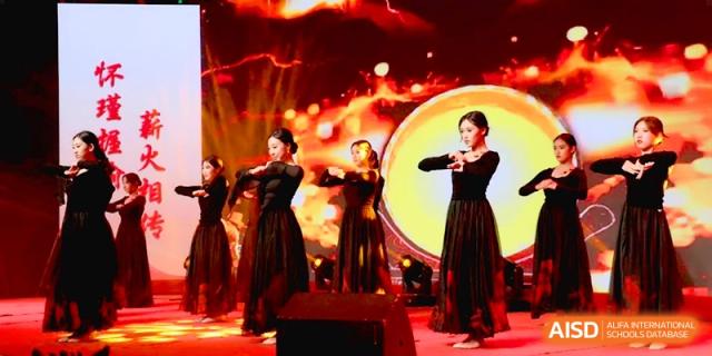 A group of female dancers in long black and red dresses performs a synchronized routine on a brightly lit stage at Baoji Nanshan High School.