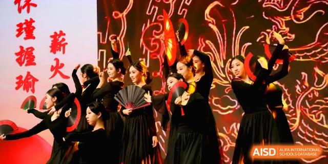 Students dressed in elegant black traditional costumes with fans perform a dramatic dance on stage at Baoji Nanshan High School.