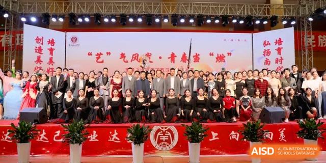 A large group of students and faculty members in formal attire pose for a commemorative group photo on a decorated stage at Baoji Nanshan High School.