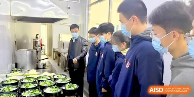 Students wearing face masks stand in the school kitchen while an official inspects the food preparation area at Baoji Nanshan High School.
