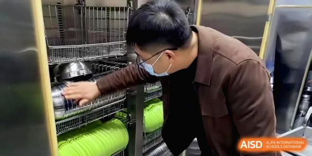 A student wearing a mask carefully organizes clean green trays in the cafeteria kitchen during a health inspection at Baoji Nanshan High School.