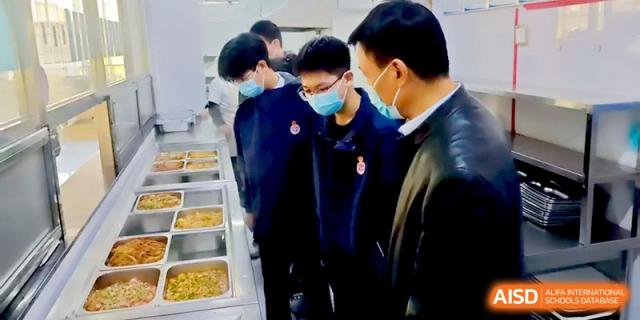 Students and an official stand by the cafeteria serving line to ensure food quality and nutritional standards at Baoji Nanshan High School.