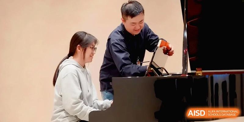 A teacher assists a student playing the piano by adjusting the sheet music stand at Beijing Eastbank Academy of Music.