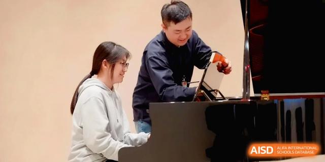 A teacher assists a student playing the piano by adjusting the sheet music stand at Beijing Eastbank Academy of Music.