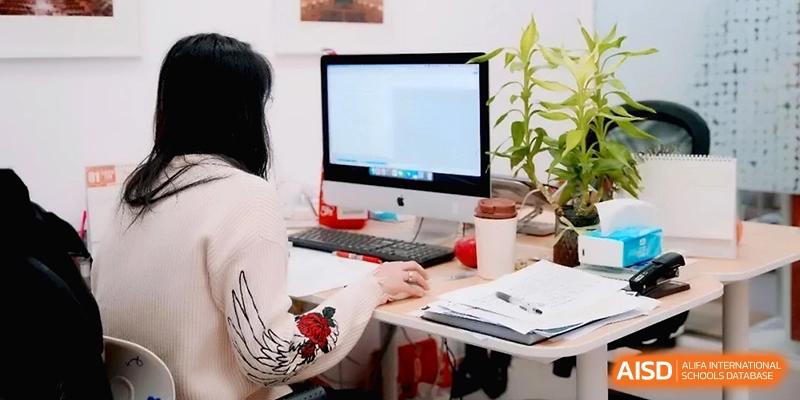 A student sits at a desk working on a computer next to a notebook and a potted plant at Beijing Eastbank Academy of Music.