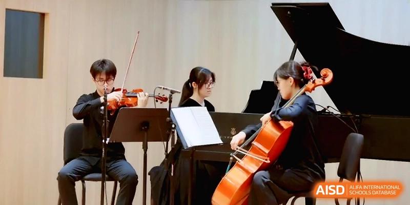 Students perform together in a small ensemble featuring a violin, cello, and piano at Beijing Eastbank Academy of Music.