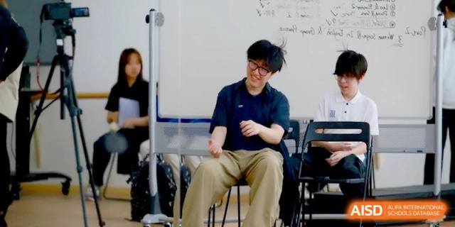 A young man in a navy shirt and glasses laughs during an interactive group session in a classroom at Beijing Eastbank Academy of Music.