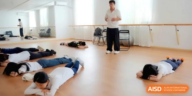 A group of students lies on the floor of a studio while an instructor speaks at Beijing Eastbank Academy of Music.