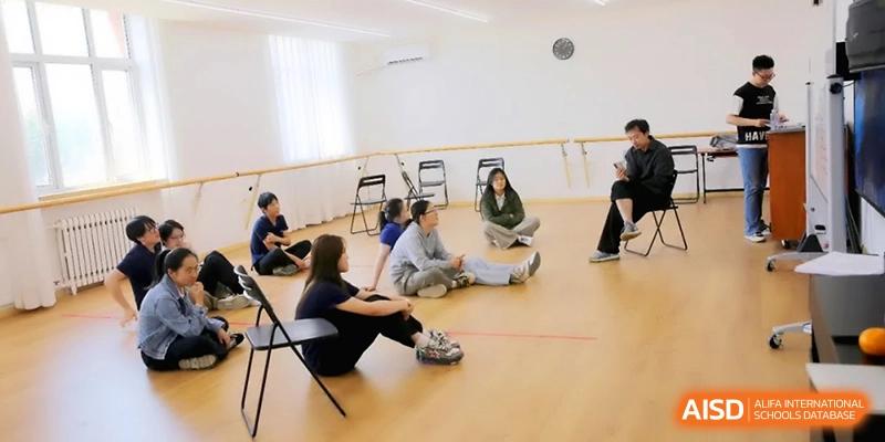 Students sit in a circle on the floor of a dance or movement studio during a workshop at Beijing Eastbank Academy of Music.