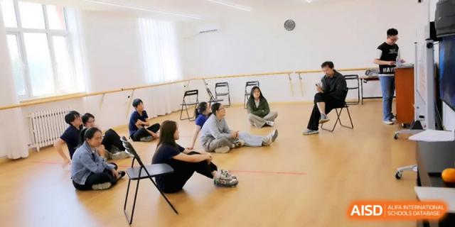 Students sit in a circle on the floor of a dance or movement studio during a workshop at Beijing Eastbank Academy of Music.
