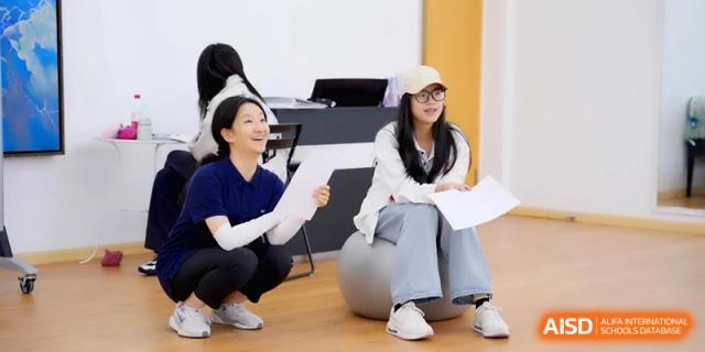 Two female students smile and interact while sitting on exercise balls in a lounge at Beijing Eastbank Academy of Music.