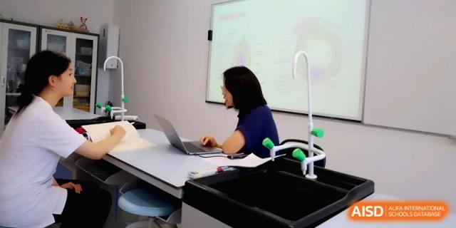 A teacher works on a laptop at a desk in front of a projection screen at Beijing Eastbank Academy of Music.