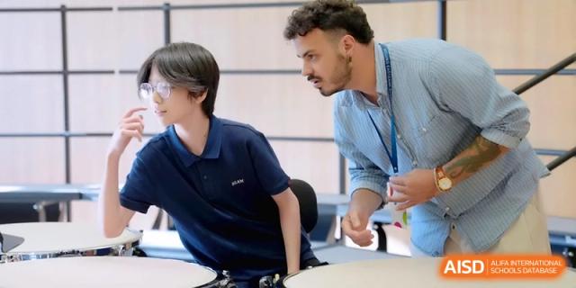 A male teacher leans over a desk to provide one-on-one guidance to a student at Beijing Eastbank Academy of Music.