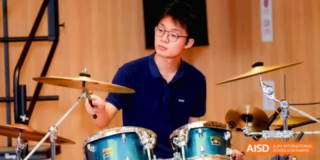 A male student focuses intently while playing the drums during a music lesson at Beijing Eastbank Academy of Music.