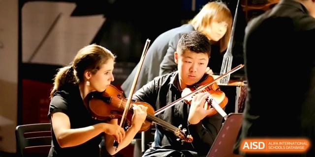 Close-up of a young male and female student focused on playing their violins during a rehearsal at Beijing Eastbank Academy of Music.