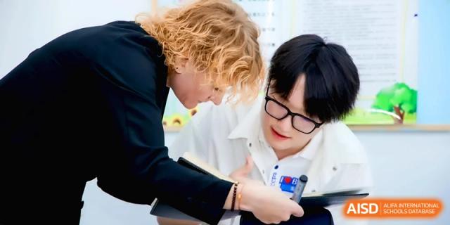 An instructor with blonde hair leans in to help a student with their music theory at Beijing Eastbank Academy of Music.