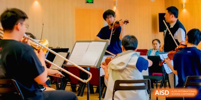 A student plays the violin in a rehearsal hall with other musicians in the background at Beijing Eastbank Academy of Music.