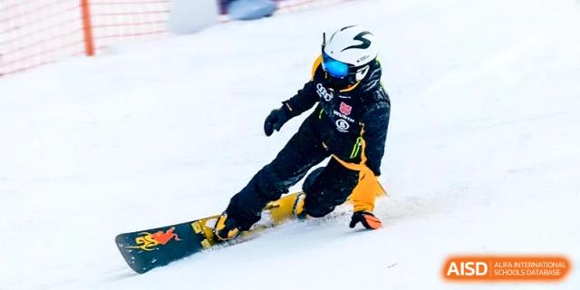 A student in full winter gear and a helmet practices snowboarding on a snowy slope at Beijing Eastbank Academy of Music.