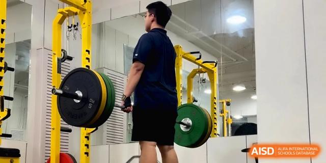A student athlete performing a heavy barbell deadlift during a training session in the gym at Beijing Eastbank Academy of Music.