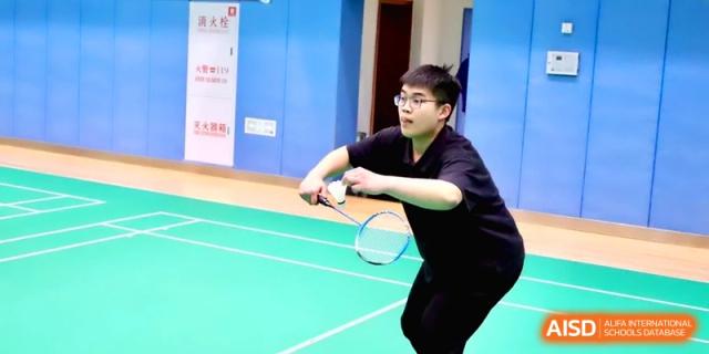 A young male student focused on a badminton match, holding his racket ready on the court at Beijing Eastbank Academy of Music.