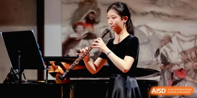 A female student in a black dress playing the oboe during a solo performance at Beijing Eastbank Academy of Music.