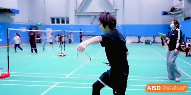 A student athlete swinging a badminton racket during a fast-paced indoor match at Beijing Eastbank Academy of Music.
