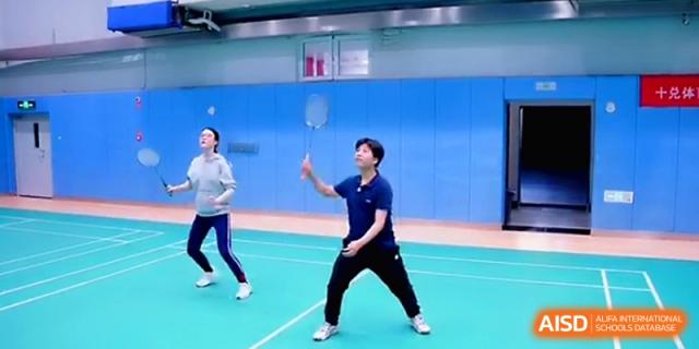 Two students actively engaged in a competitive badminton game on an indoor court at Beijing Eastbank Academy of Music.