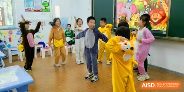 Children dressed in various animal costumes including lions and bears perform a lively dance routine on a wooden floor in a classroom at Beijing Haidian Rising Experimental School