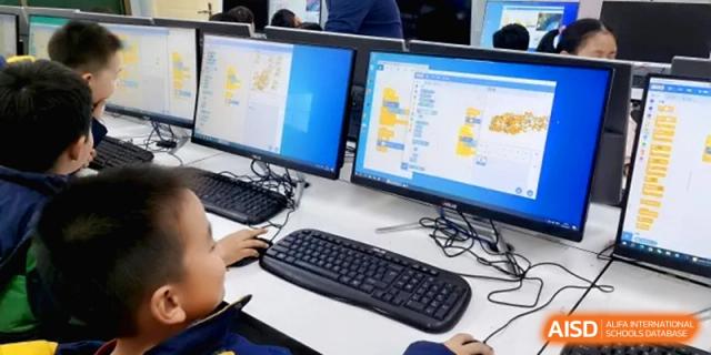 A close-up view of a student using a computer keyboard and mouse to work on a coding project displayed on dual monitors in a computer lab at Beijing Haidian Rising Experimental School