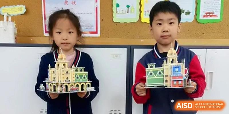 Two students hold up intricate architectural models they have built from blocks, showcasing their creative engineering projects in class at Beijing Haidian Rising Experimental School