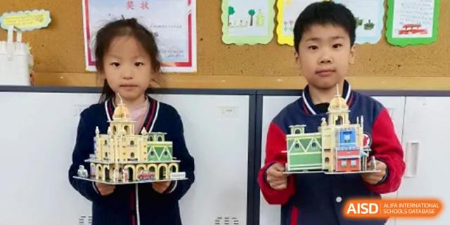 Two students hold up intricate architectural models they have built from blocks, showcasing their creative engineering projects in class at Beijing Haidian Rising Experimental School