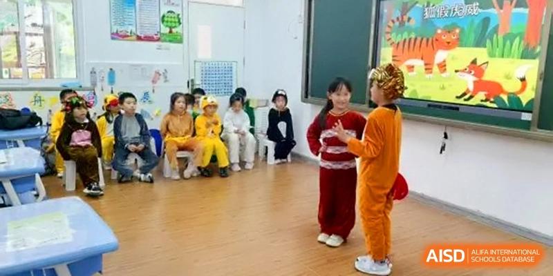 Two young students in animal costumes perform a playful skit on a wooden floor in front of their seated classmates at the Beijing Haidian Rising Experimental School